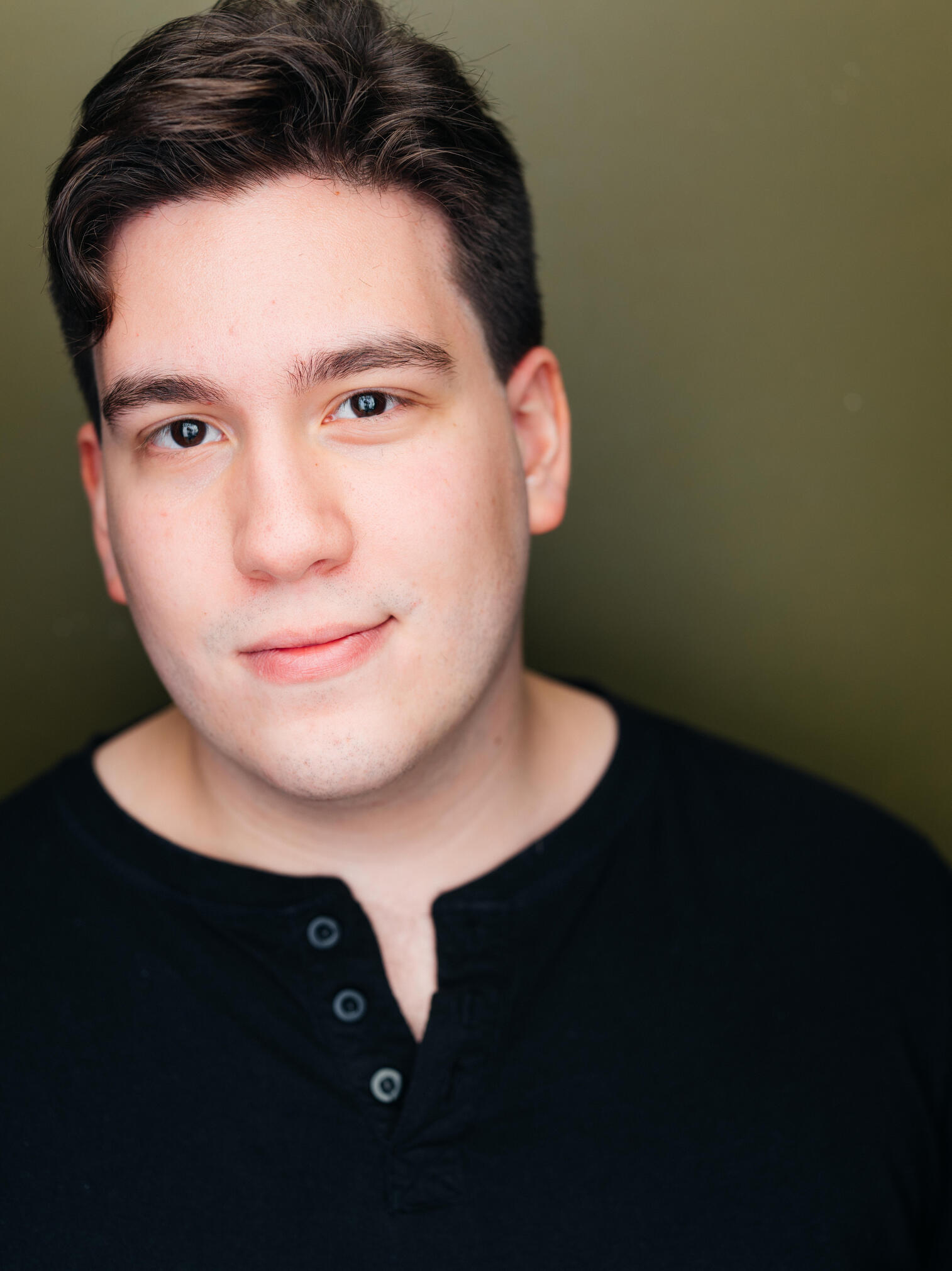 Headshot of Dennis Oliveira. Image of a brown eyed, brown haired, clean shaven latino man in a black henley against a dark green background.
