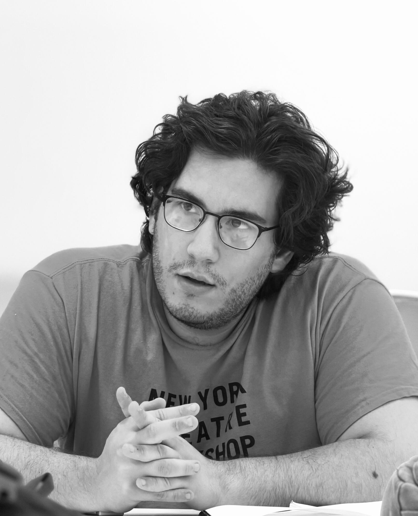 Headshot of Dennis Oliveira. Image of a brown eyed, brown haired, clean shaven latino man in a black henley against a dark green background.